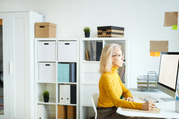 Side view portrait of elegant mature businesswoman working with computer while sitting at desk in...