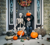 Portrait of smiling holding pumpkin while sitting with skeleton at doorway during Halloween