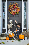 Smiling boy giving high-five to skeleton while sitting against door during Halloween