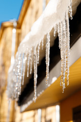 Building covered with icicles in sunny winter day, closeup. Ice stalactite hanging from roof, soft focus. Icicle formation on the sunny side. Thaw, early spring weather concept
