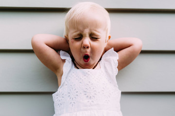 Cute girl with hands behind head yawning while standing against wall