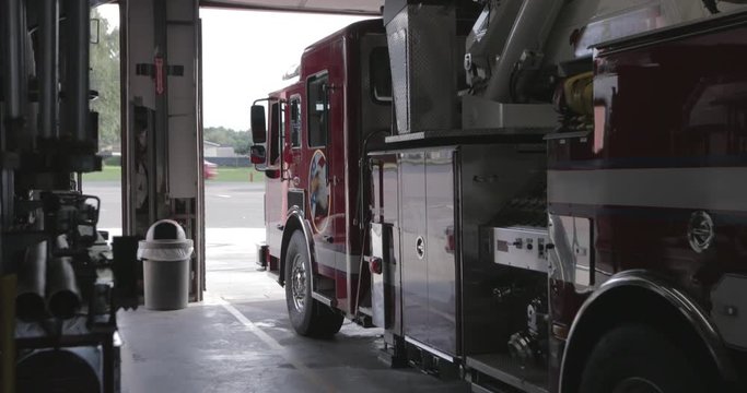 Firefighters stand near a red fire engine inside a fire department prepared to respond to an emergency