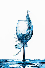 Clear Wineglass With Bluish Water Splash and Drops In Motion Against Pure White Background.
