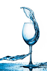Clear Wineglass With Bluish Water Splash In Motion Against Pure White Background.