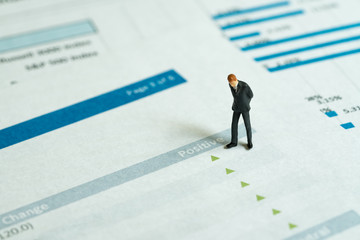 Miniature businessman looking at green pointing up arrows of investment report, stock price go up, positive sentiment, good sign of situations in which some financial assets gain value