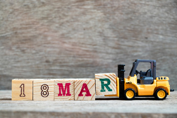 Toy forklift hold block R to complete word 18mar on wood background (Concept for calendar date 18 in month March)