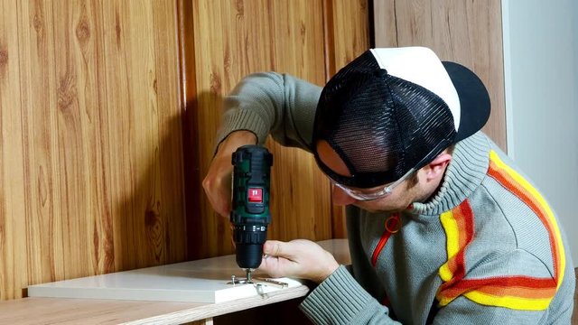Furniture installer assembling drawer with electric screwdriver. Wearing safety glasses.