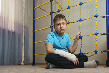 Sad child with a broken arm in the home environment . The cast on the hand of a little boy.