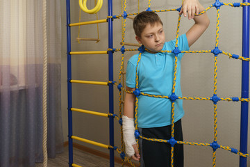 Sad child with a broken arm in the home environment . The cast on the hand of a little boy.