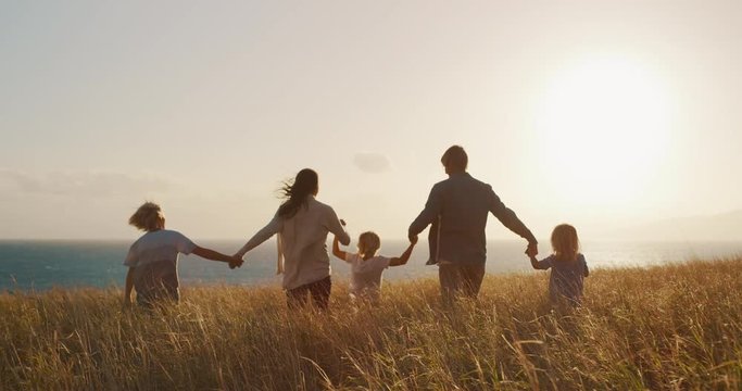 Happy family swinging child into the air, looking out to the sunset together in golden field by the ocean