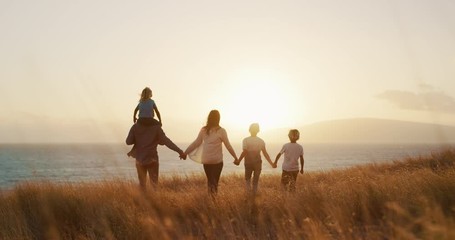 Happy family walking in golden field and looking out to the sunset together by the ocean