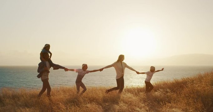 Happy family holding hands and walking through golden grass together at sunset by the ocean