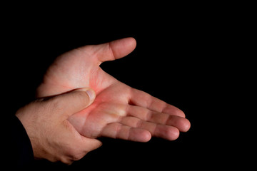 Man's hands with pain in the palm of the hand. Massage in the palm with the thumb. Hands of young white man, on black background.