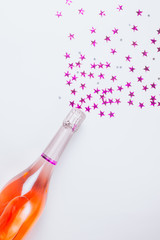 Champagne bottle with confetti stars on white background.