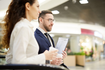 Fototapeta premium Young businessman with document and drink and his colleague discussing what they are looking at in the mall