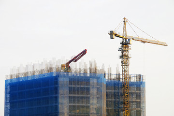 Fototapeta na wymiar Top of big under construction building of concrete and steel structure with yellow crane and excavator truck on white sky background