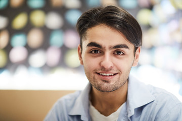 Obraz premium Young smiling handsome man in light blue shirt looking at you while sitting in front of camera in cafe