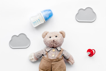 Feed baby concept. Teddy bear toy near small bottle with food on white background top view