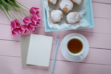 Spring tea.Flat lay.Spring to-do list.pink tulips flowers,  blank notebook, cup of tea and  blue tray with donuts on a pink wooden background.top view, copy space.Spring mood