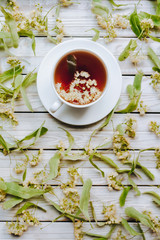 White cup and dish of linden tea on linden blossom background. Herbal medicine concept. Top view. Rustic style.