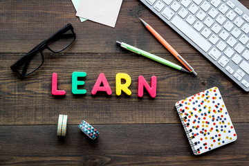 Learn concept. Word learn lined with colorful letters near computer keyboard and stationery on dark wooden background top view