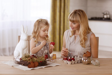 Mother and daughter paint Easter eggs in the room at the holiday table.