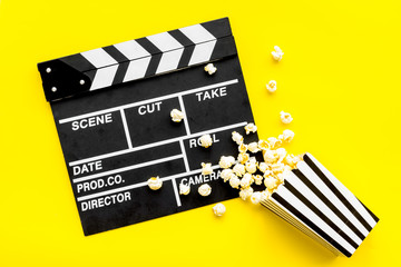 Movie premiere concept. Clapperboard and popcorn on yellow background top view