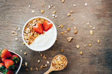 Top view of yogurt in a wooden bowl with granola,fresh strawberry on white wooden table. Health food concept.