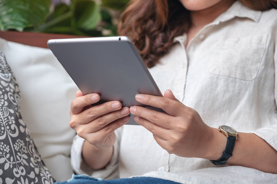 Closeup image of a woman holding and using tablet pc while sitting on sofa