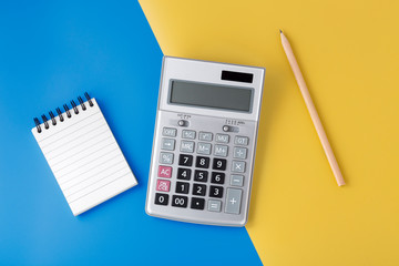 Sliver calculator on yellow and blue background with notepad and pencil