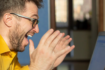 A bearded man with glasses looks at the laptop screen in amazement.