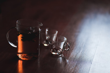 Hot herbal brewed tea in transparent teapot and two cupson wooden background.