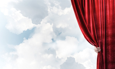 Cloudy landscape behind red curtain and hand holding it