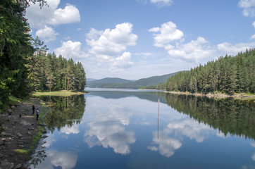 Lake Shiroka Polyana in the Rhodopes  with reflections of pines and clouds, Bulgaria