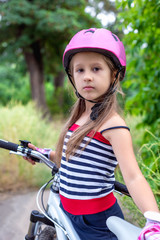 Fototapeta na wymiar Little cute girl in a pink helmet near a bicycle