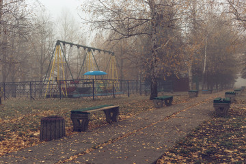 Fototapeta na wymiar Benches in an old abandoned amusement park on a foggy autumn morning