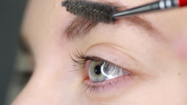 Close up of blue eye and brush putting gel on eyebrow