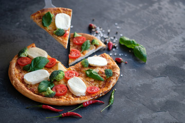 Sliced pizza with Mozzarella cheese, tomatoes, broccoli, Spices and fresh basil. Italian pizza. Pizza on black stone background
