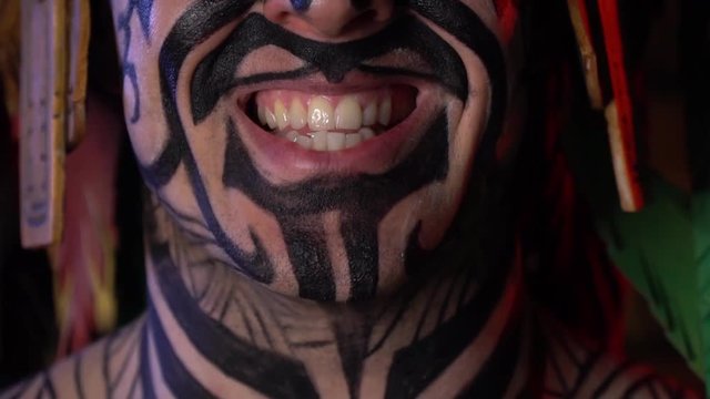 Tribal man with black paint on his face and body, talking, close up of his mouth
