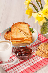 Toasted slices of bread with cheese , cup of coffee, bowl with jam and bouquet of daffodils.