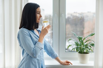 Young woman morning at home near the window drinking water with lemon, vitamin drink in winter spring season