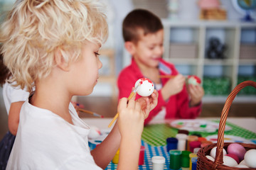 Obraz premium Side view of focused boy painting easter egg