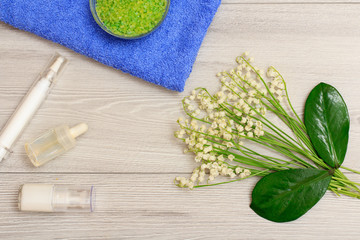 Bottles with cream for face skin and aromatic oil, bowl with sea salt on towel, green leaves and bouquet of lilies of the valley.