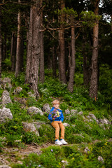 Boy with glasses and blue wear with bouquet of wild flowers in the summer mountains. Flowers for mother and sister for the woman's day.