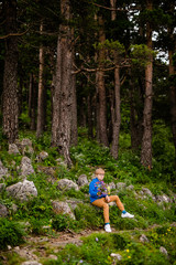 Boy with glasses and blue wear with bouquet of wild flowers in the summer mountains. Flowers for mother and sister for the woman’s day.