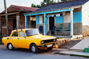 Yellow vintage Cuban car parked in front of tropical home in rural Cuba