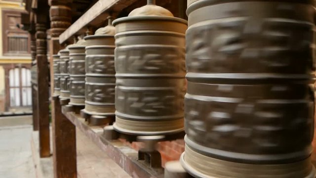 Row of aged religious prayer wheels or drums with mantra Om Mani Padme Hum in yard of temple, Durbar Square, Nepal, Kathmandu. Tibetian buddhism