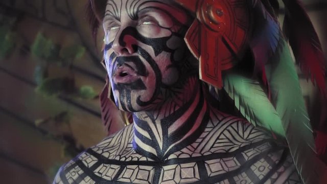 Close up of a scary tribal shaman with painted face, eating a heart at the sacrifice place