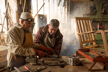 Two craftsmen in their craft workshop work metal parts 