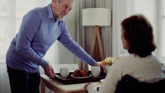 Senior couple with wheelchair sitting at the table at home, having breakfast.